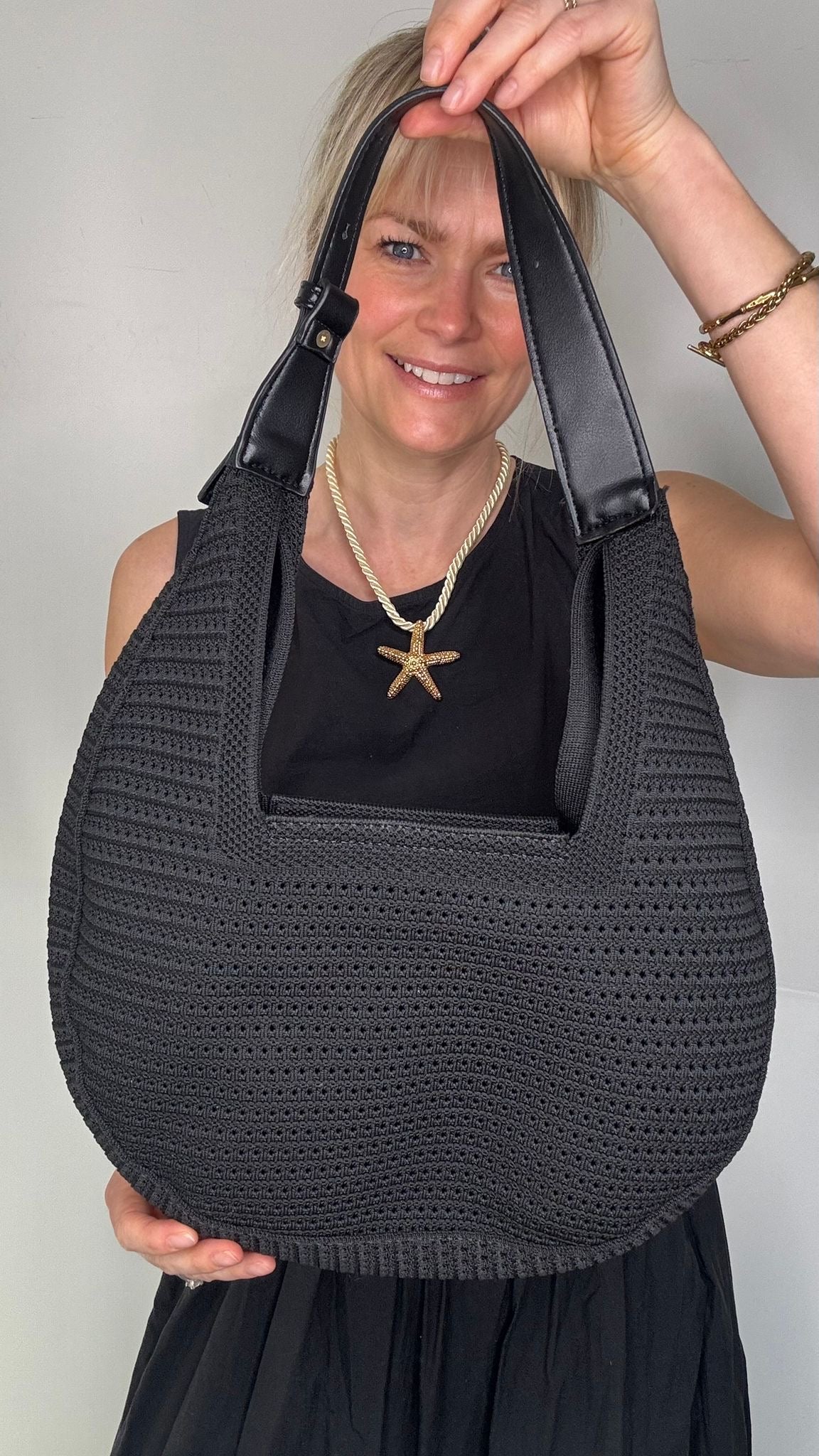 Woman wearing a black dress, holding a black woven handbag. 