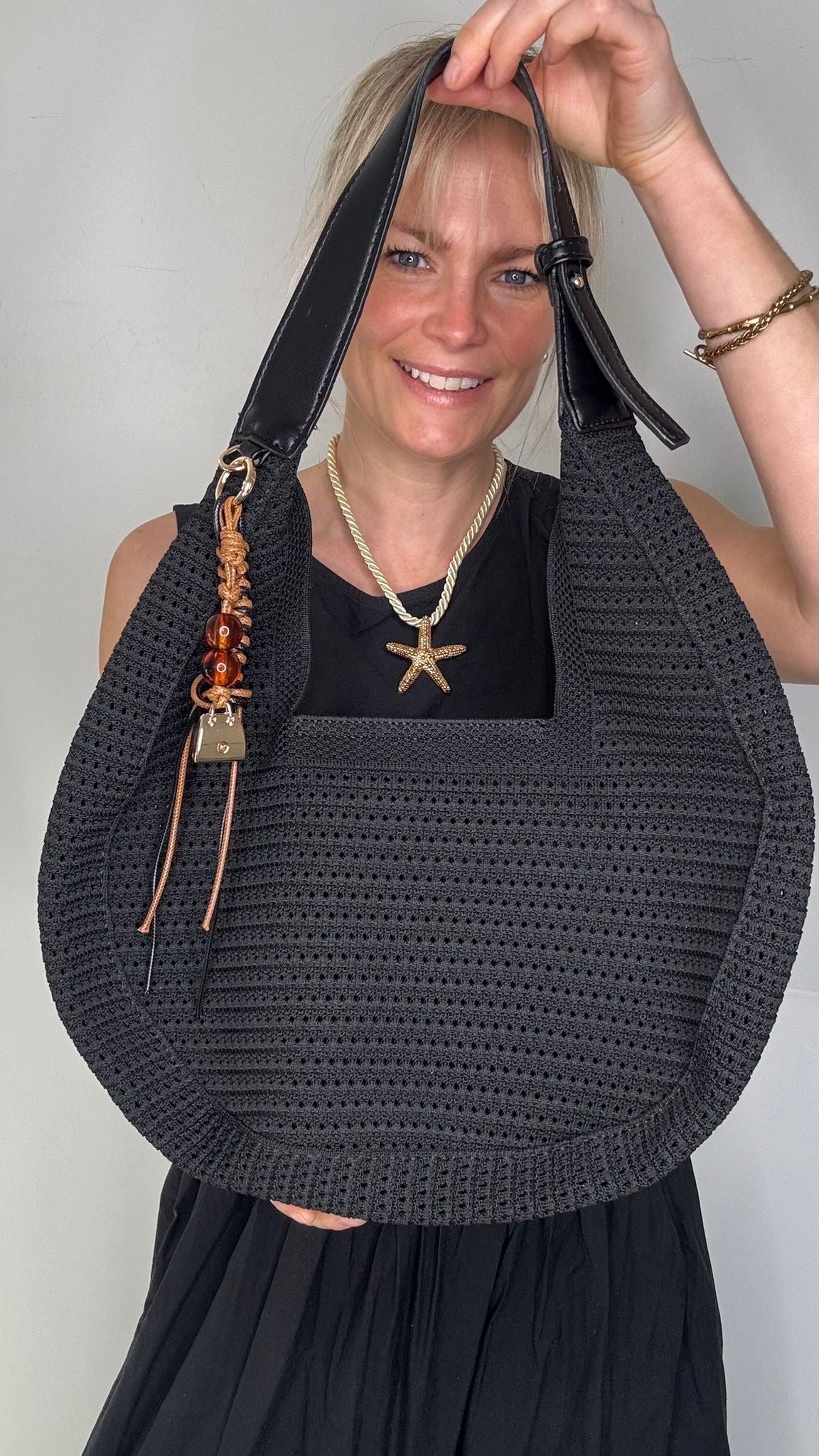 Woman wearing a black dress, holding a black woven handbag. 