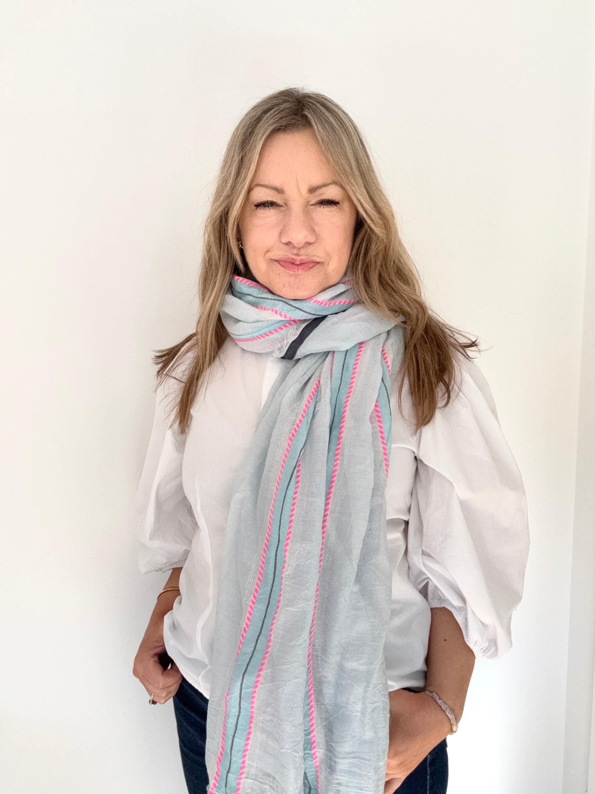 Woman wearing a blue and pink striped scarf over a white shirt. 