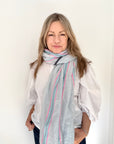 Woman wearing a blue and pink striped scarf over a white shirt. 