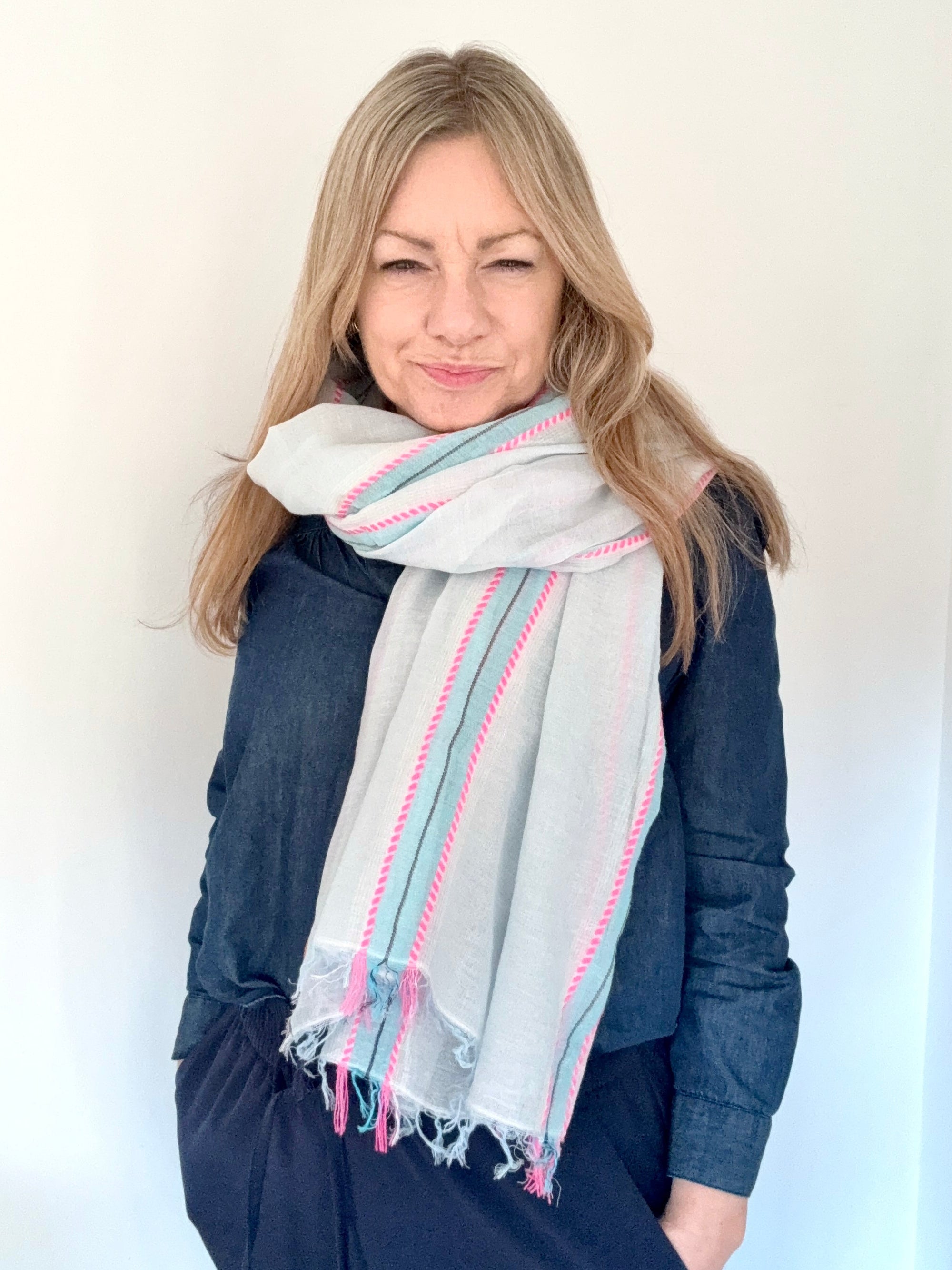 Woman wearing a light blue and pink scarf  over a blue denim shirt.
