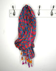 Colorful patterned scarf with tassels hanging on a white wall with hooks.