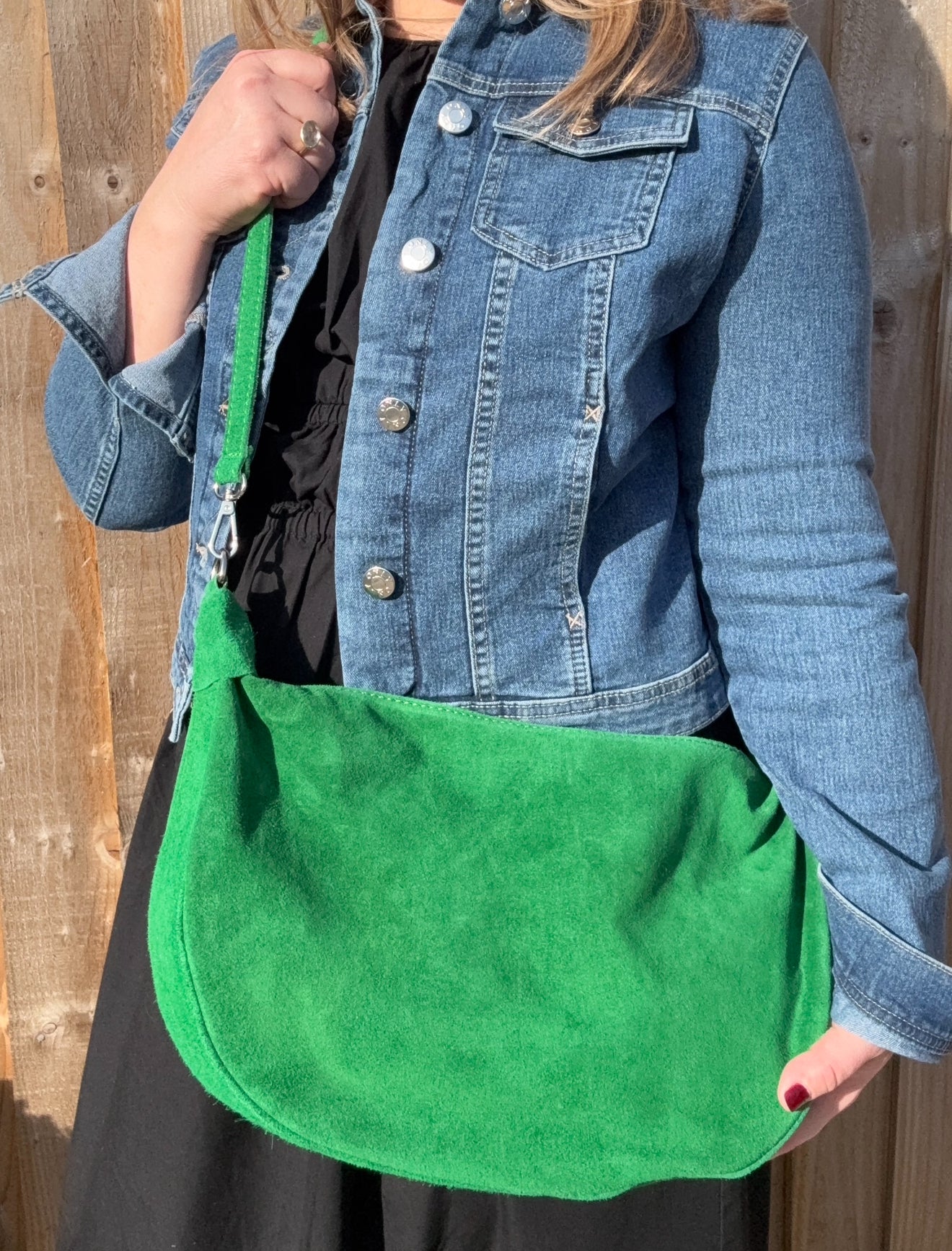 a woman wearing a denim jacket holding a bright green large crossbody swing bag 