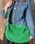 a woman wearing a denim jacket holding a bright green large crossbody swing bag 