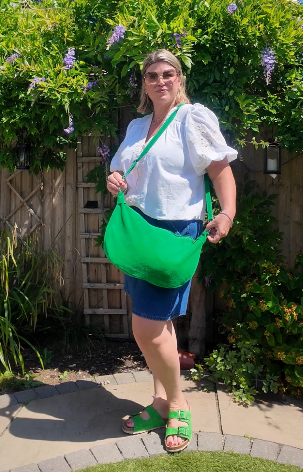 Woman holding a green bag outdoors with greenery in the background