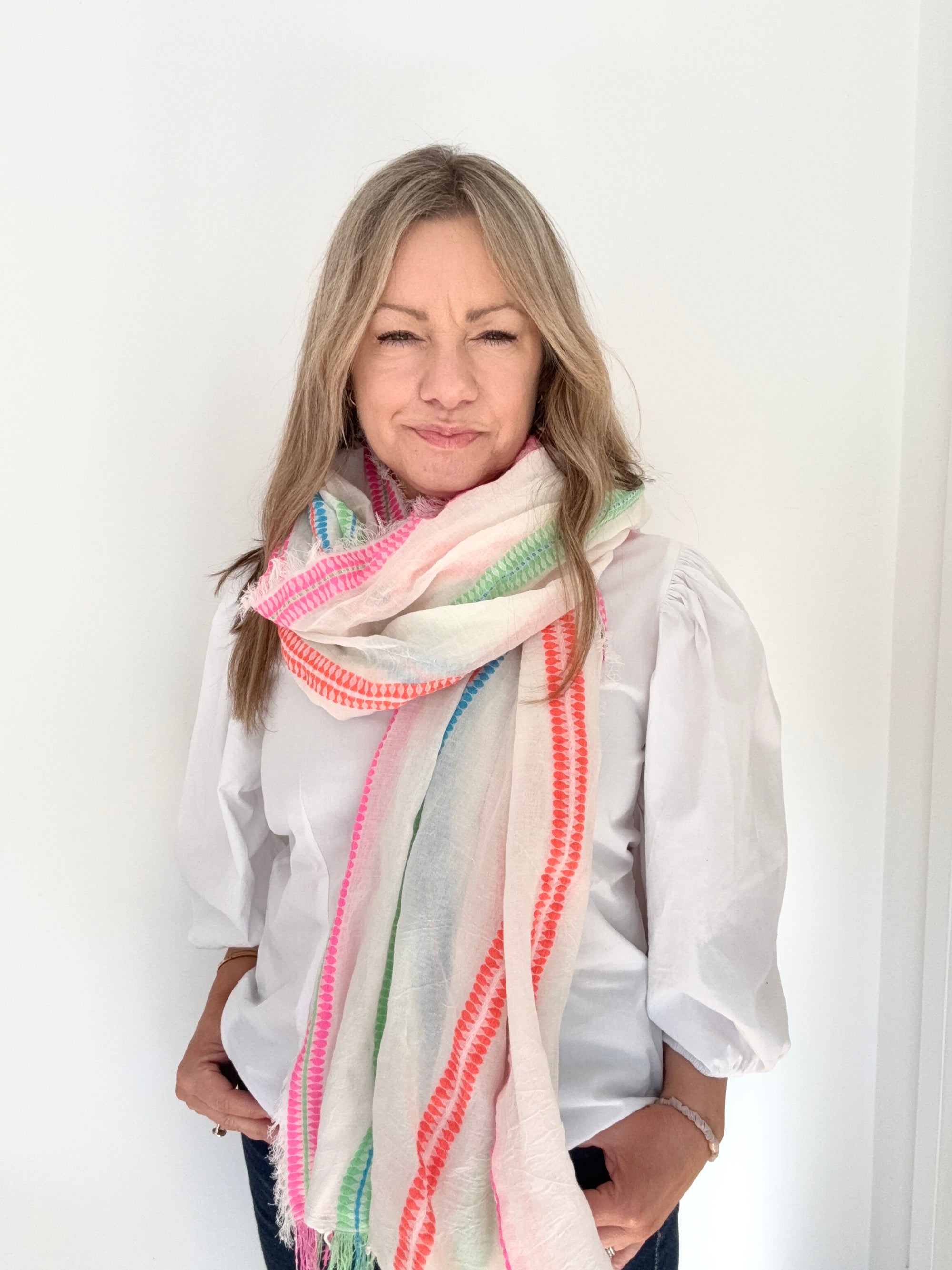 Woman wearing a white shirt and a multi-coloured scarf against a white background.