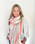 Woman wearing a white shirt and a multi-coloured scarf against a white background.