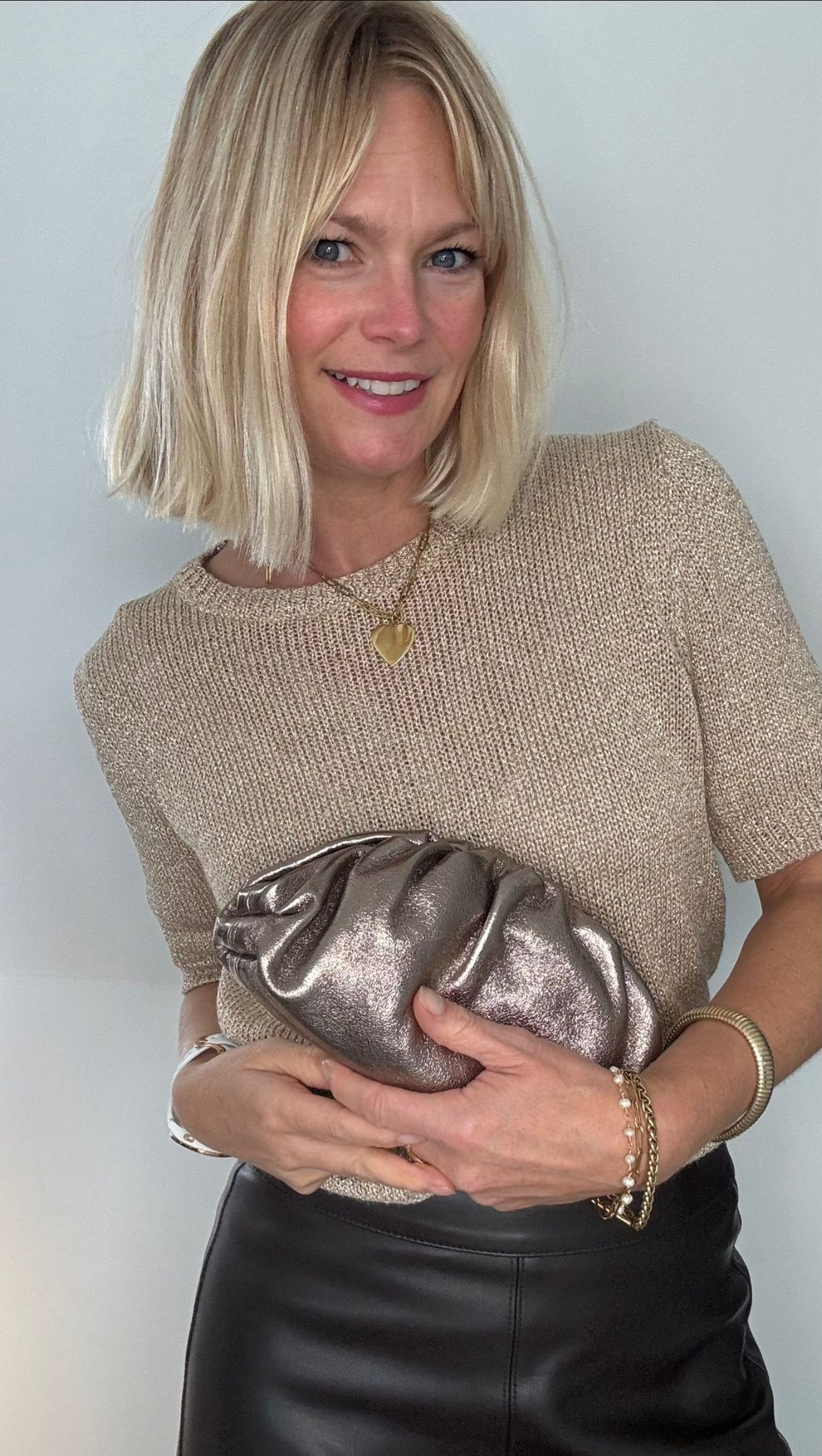 Woman wearing a beige top and black trousers, holding a bronze cloud bag.