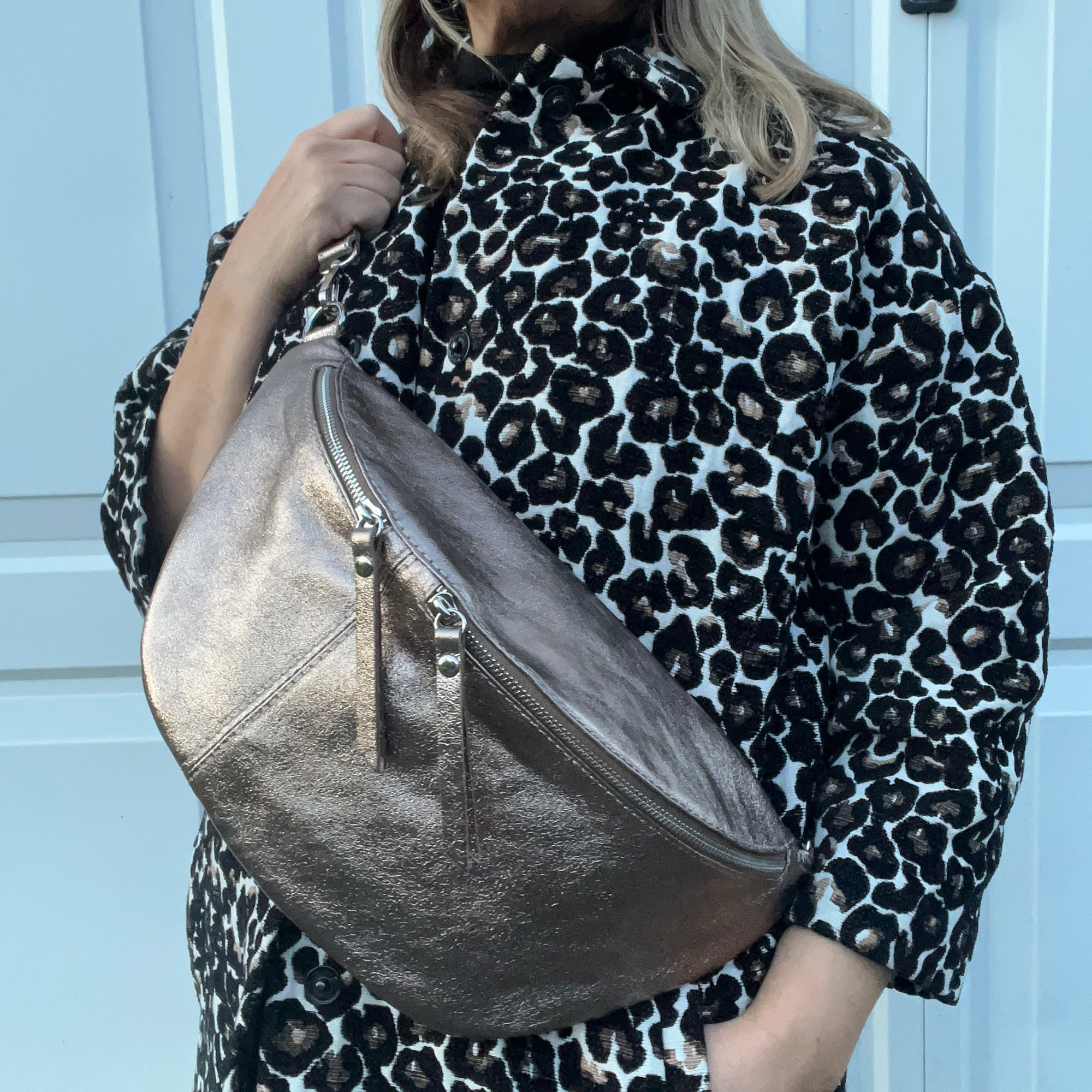 a woman wearing a leopard print jacket holding a large bronze crossbody bum bag. 