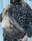 a woman wearing a leopard print jacket holding a large bronze crossbody bum bag. 