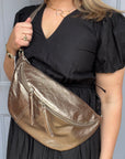 
a woman wearing a black dress holding a large bronze crossbody bum bag. 
