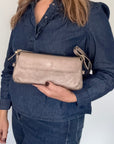Woman wearing a denim jacket holding a bronze clutch handbag against a white background.