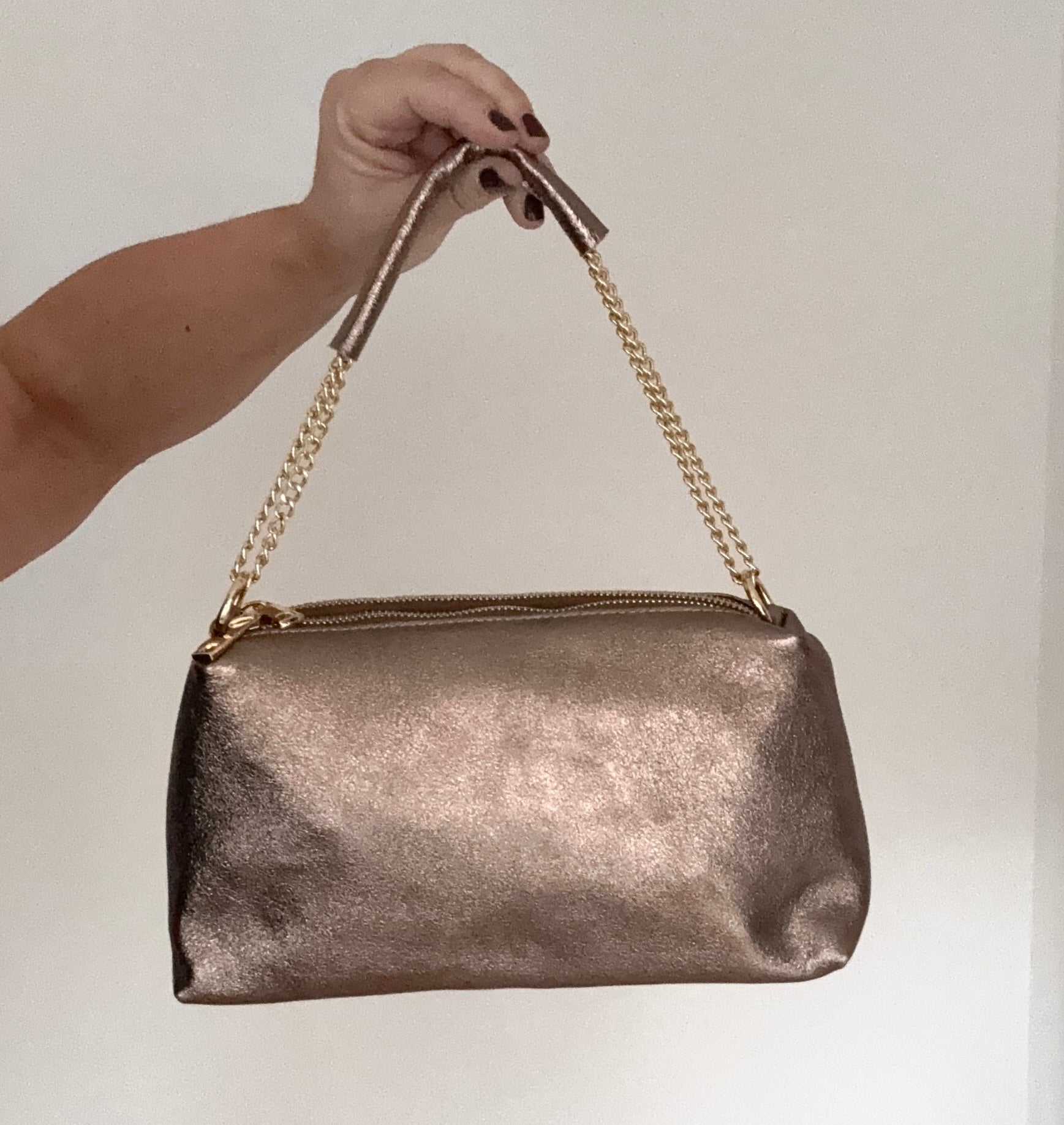 bronze leather clutch/ shoulder/ crossbody handbag with chain strap held by a hand (woman's)