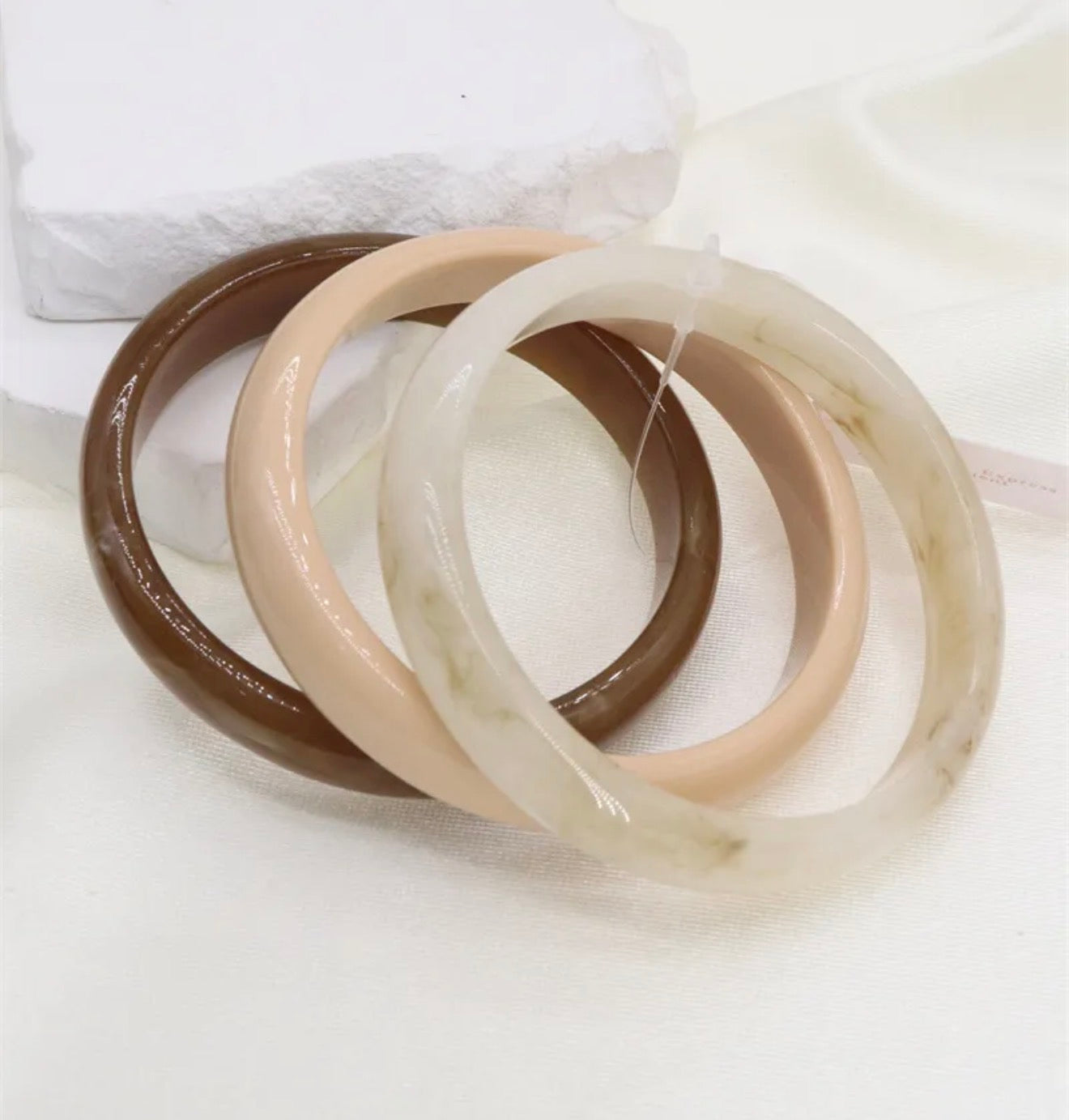 Three jade bracelets in brown, beige, and white on a white background
