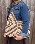 Woman wearing a denim jacket, holding a brown and cream raffia shoulder bag. 
