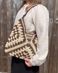 Woman wearing a white shirt, holding a brown and cream raffia shoulder bag. 