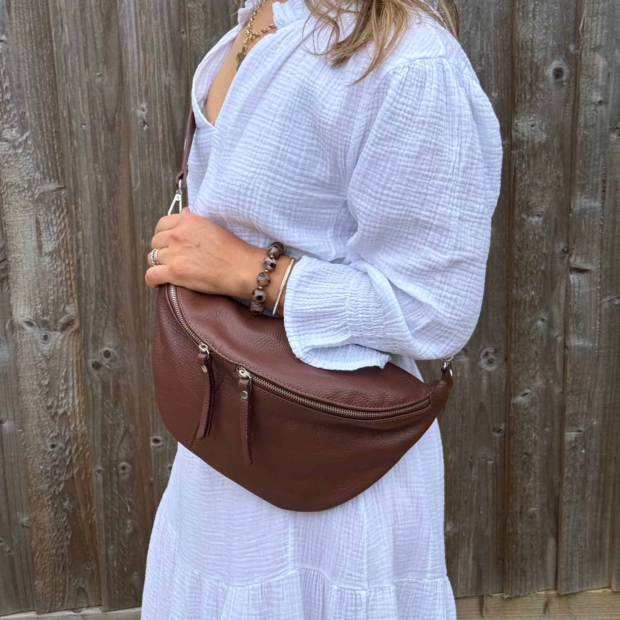 Woman wearing a white outfit holding a brown leather bag against a wooden fence.