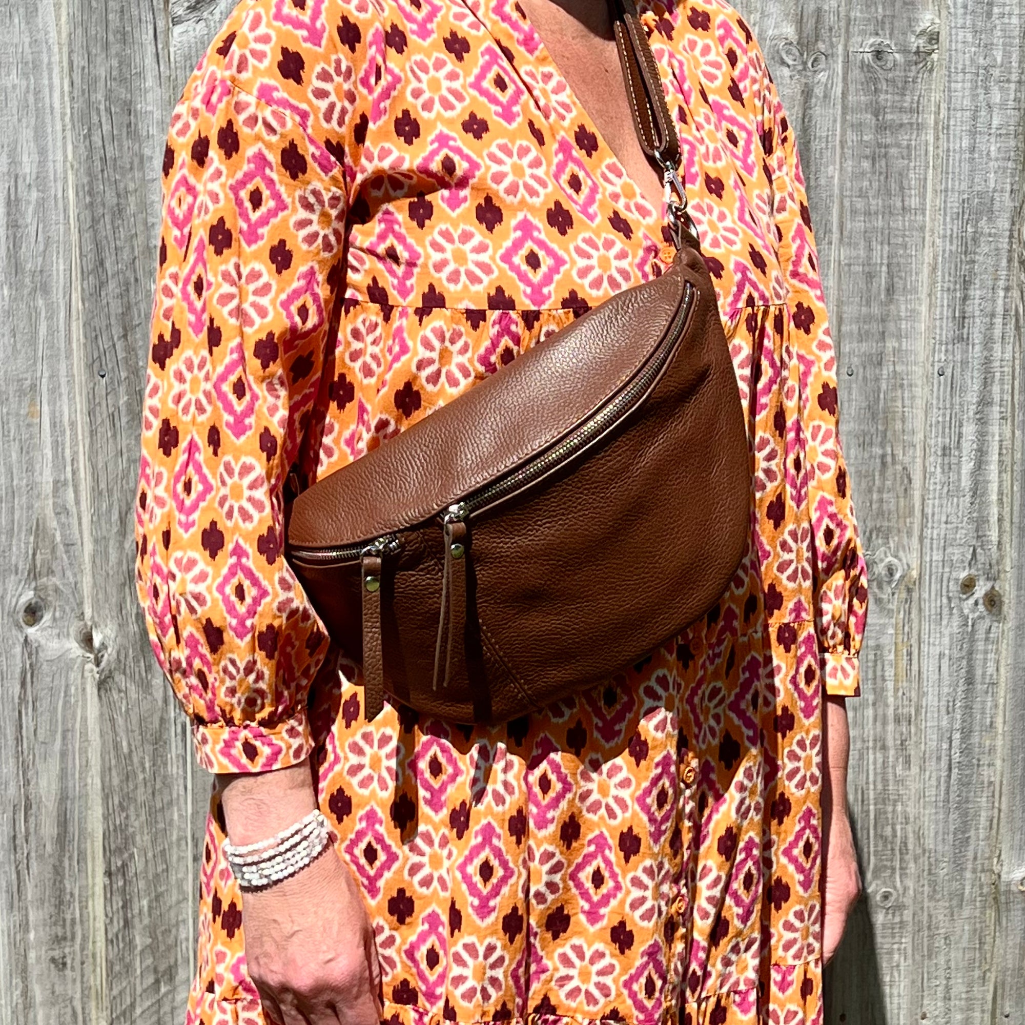 Woman wearing a floral orange dress with a brown crossbody/ bum bag 