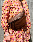 Woman wearing a floral orange dress with a brown crossbody/ bum bag 