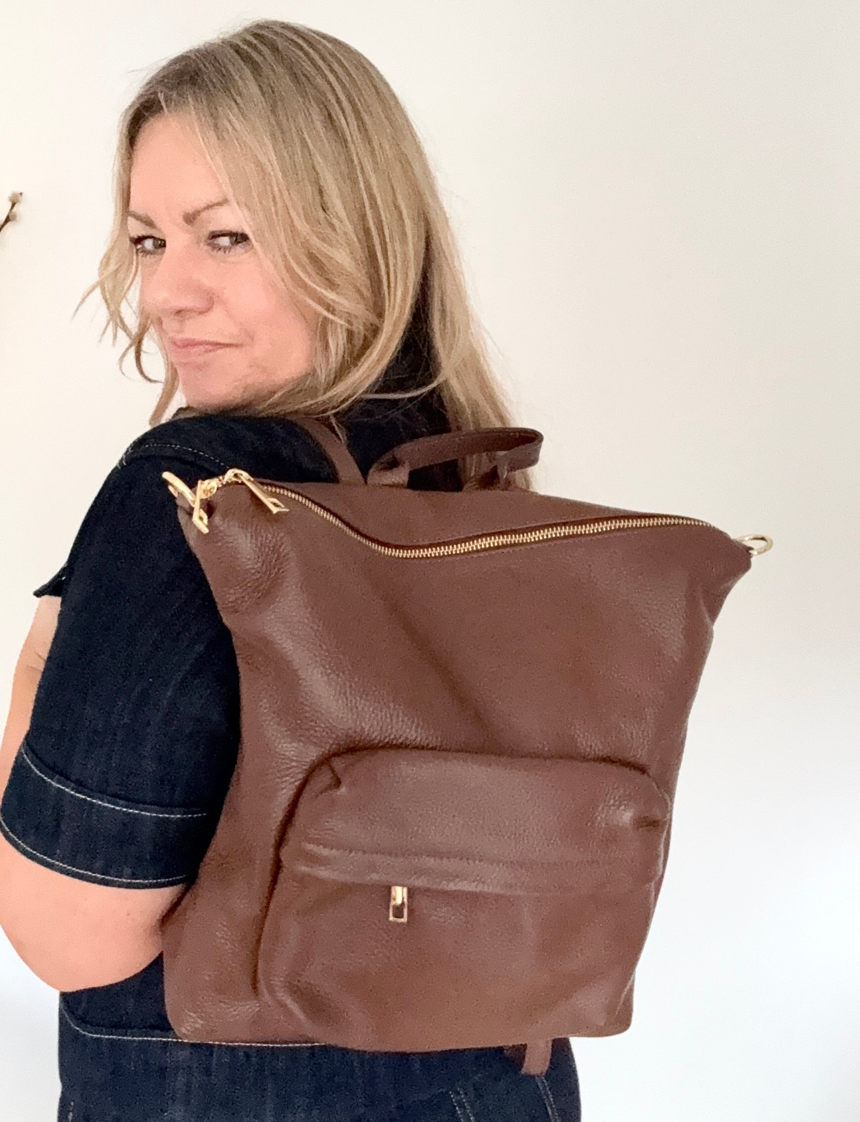 Woman wearing a brown leather backpack with gold accents and zippers 