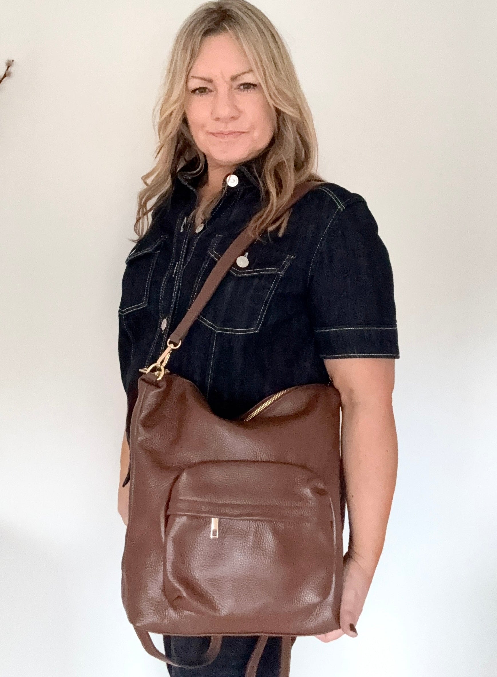 Woman holding a brown leather backpack bag with gold accents and a brown leather shoulder strap