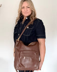 Woman holding a brown leather backpack bag with gold accents and a brown leather shoulder strap