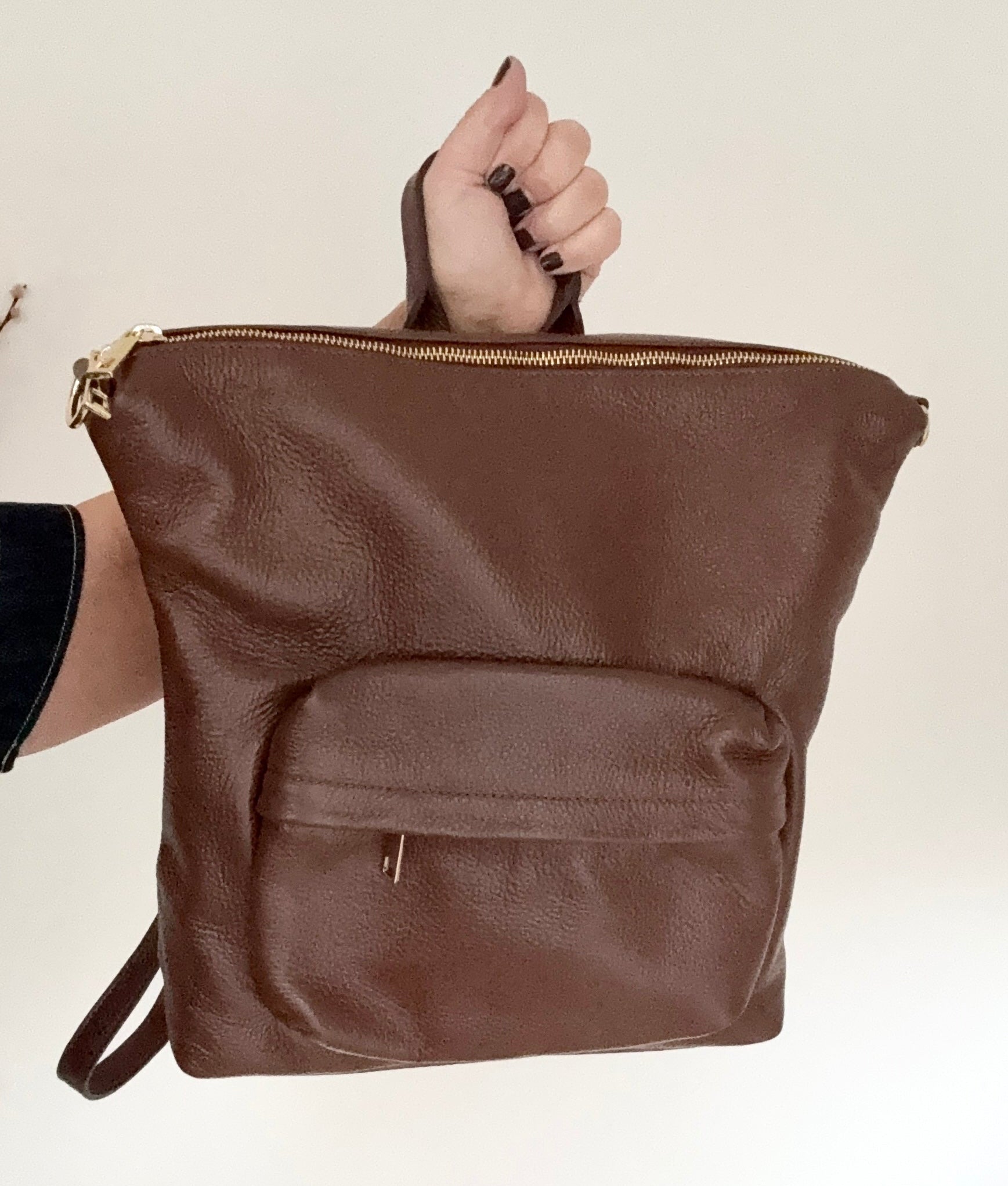 Brown leather backpack with gold accents held by a woman