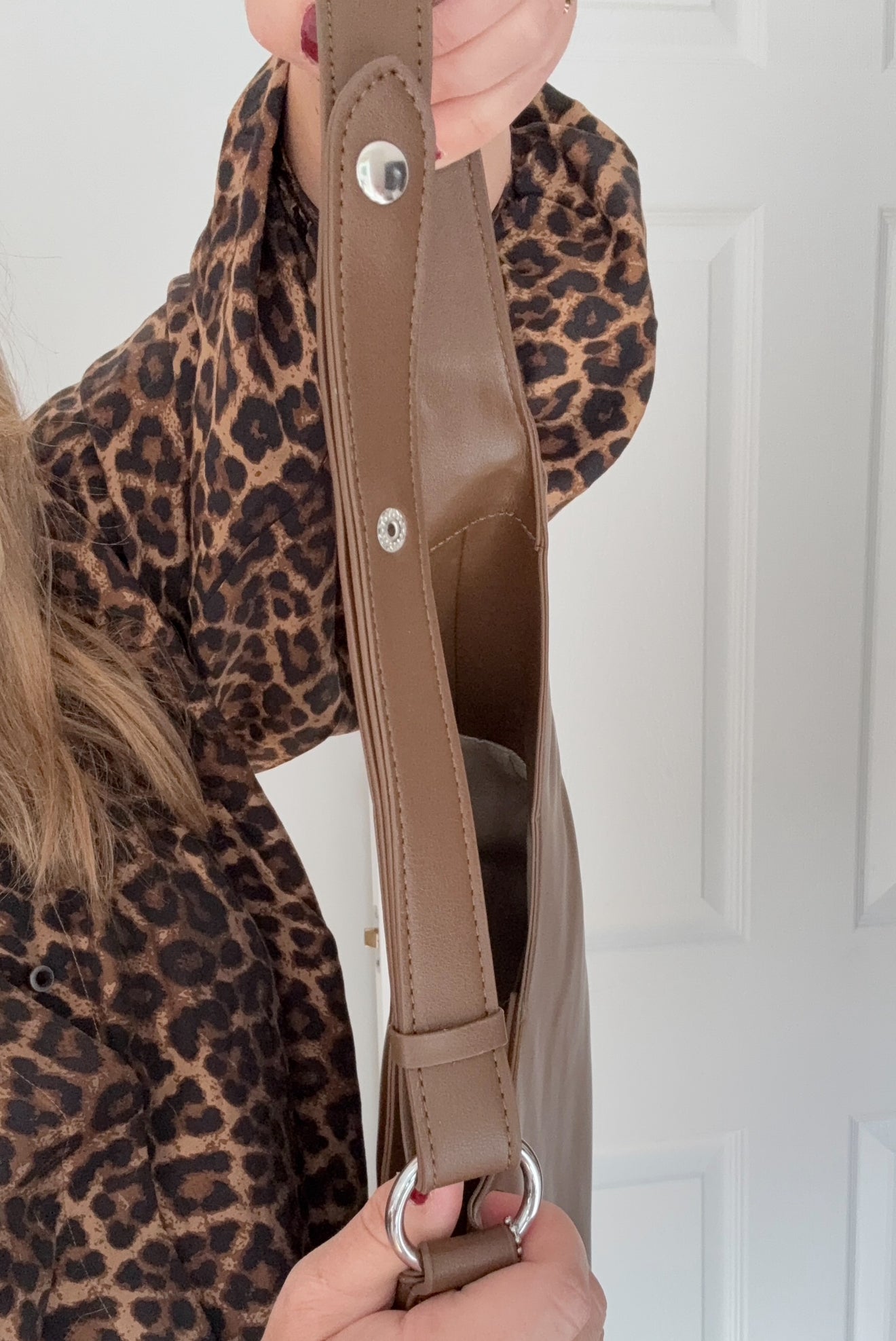Woman wearing a leopard print top holding a brown bag with silver accents
