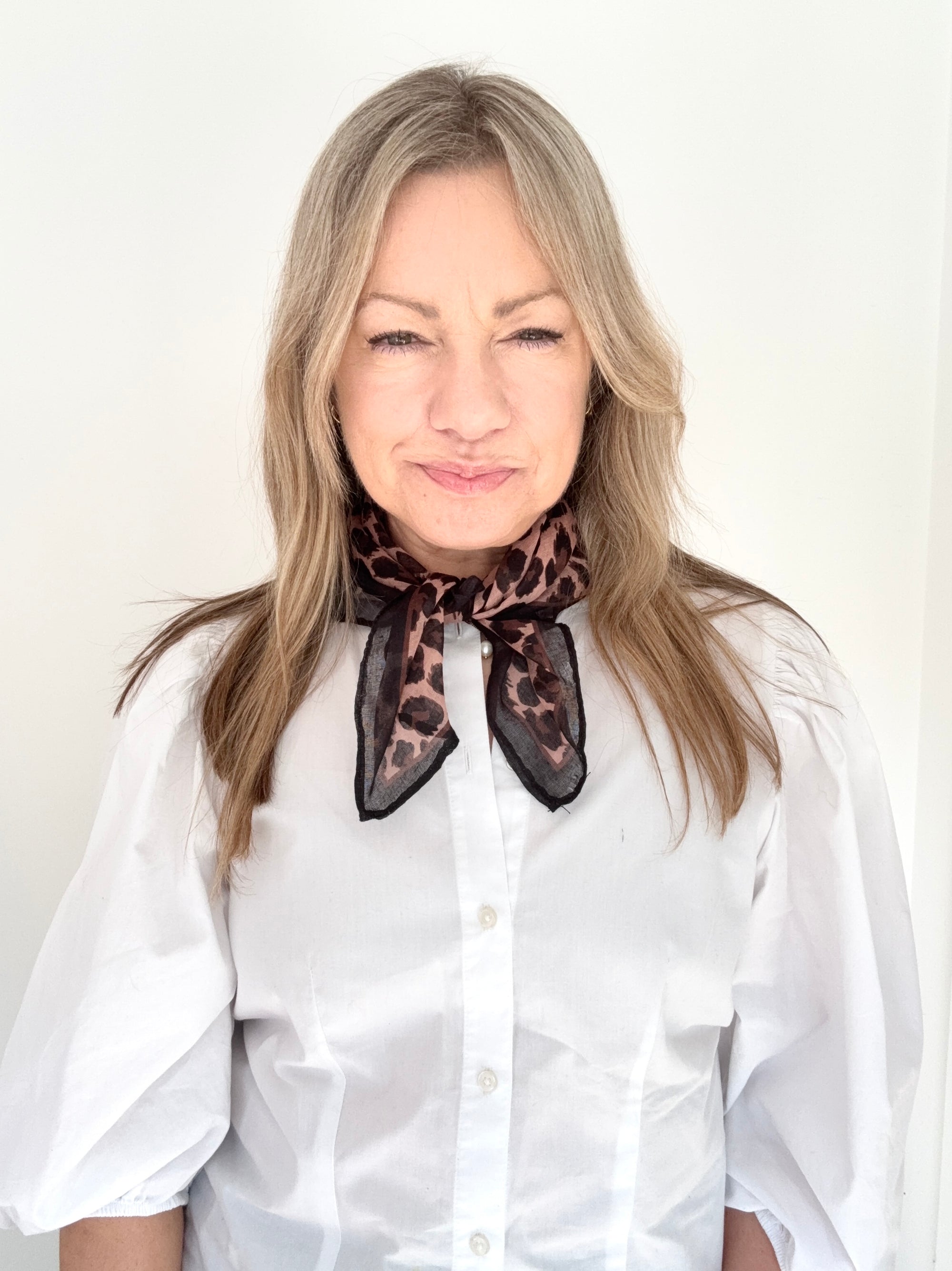 Woman wearing a white shirt and a brown animal print square scarf. 