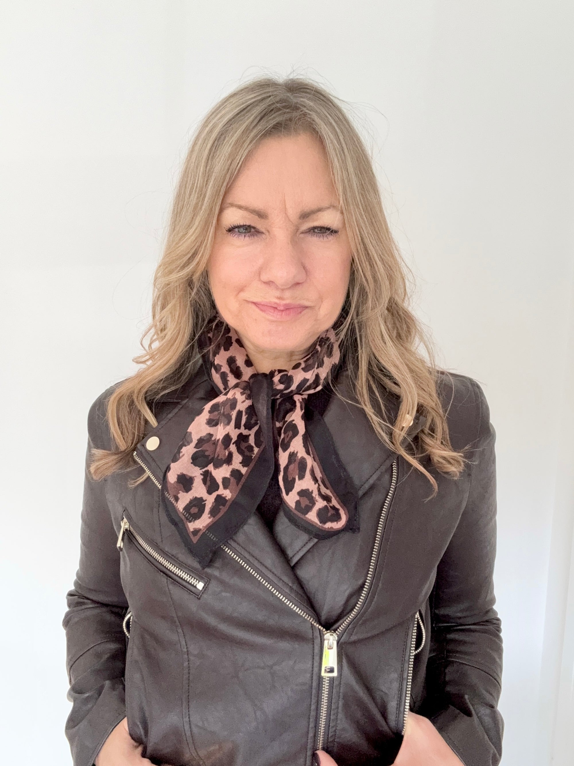 Woman wearing a grey leather jacket with a brown animal print square scarf. 