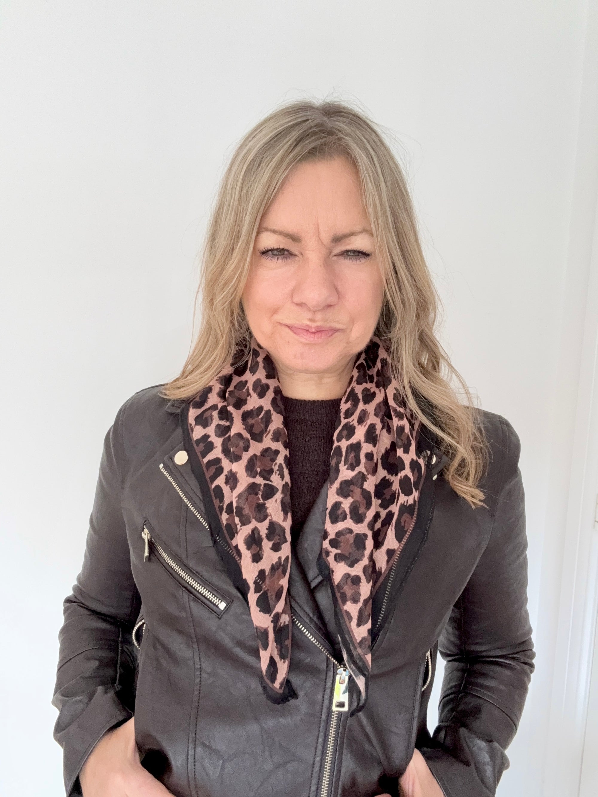 Woman wearing a grey leather jacket with a brown animal print square scarf. 