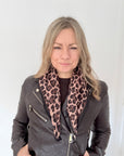 Woman wearing a grey leather jacket with a brown animal print square scarf. 