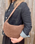 Woman wearing a denim jacket with a brown raffia shoulder bag. 
