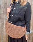Woman wearing a denim jacket with a brown raffia shoulder bag. 