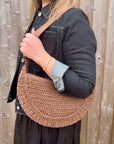 Woman wearing a denim jacket with a brown raffia shoulder bag. 