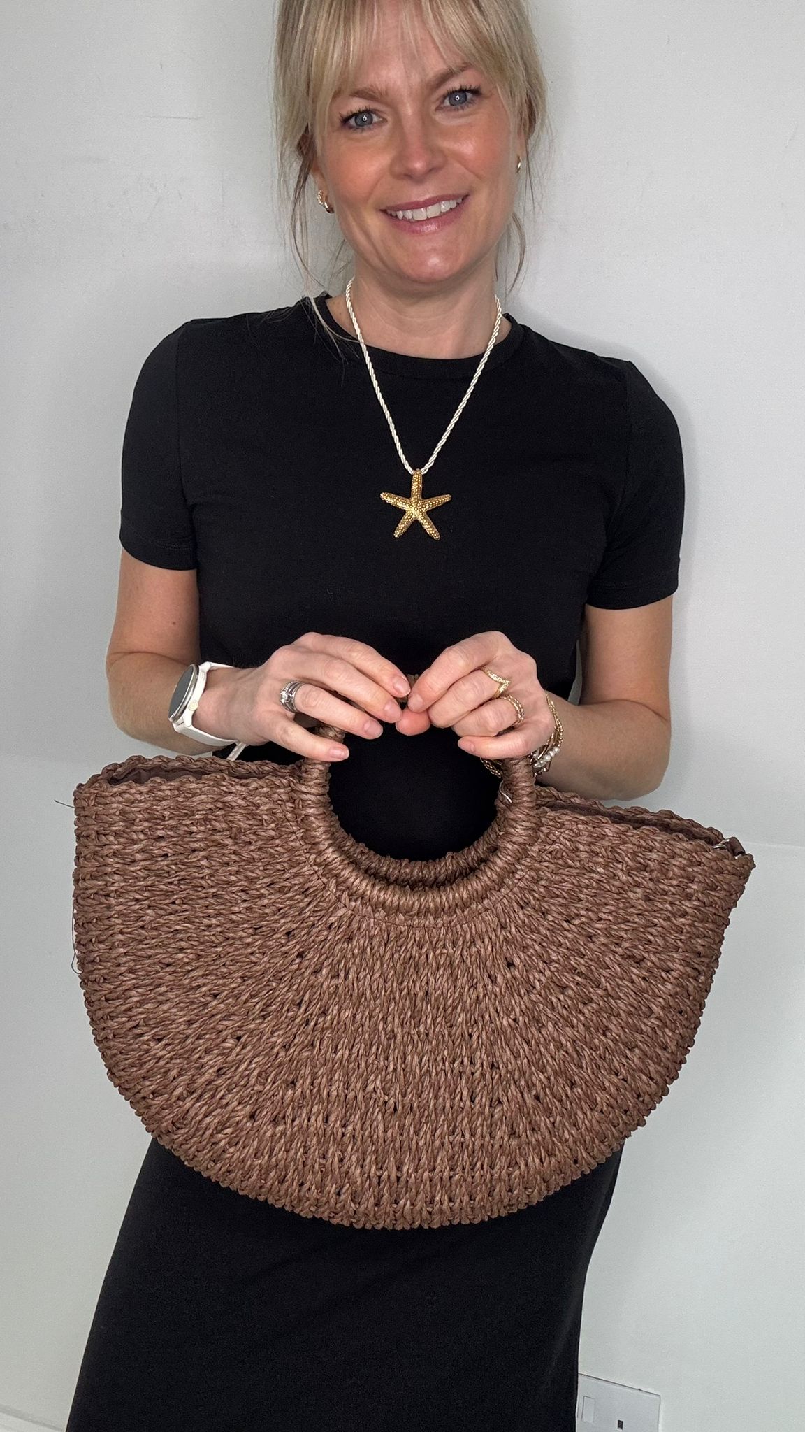 Woman wearing a black dress, holding a brown woven crossbody handbag.