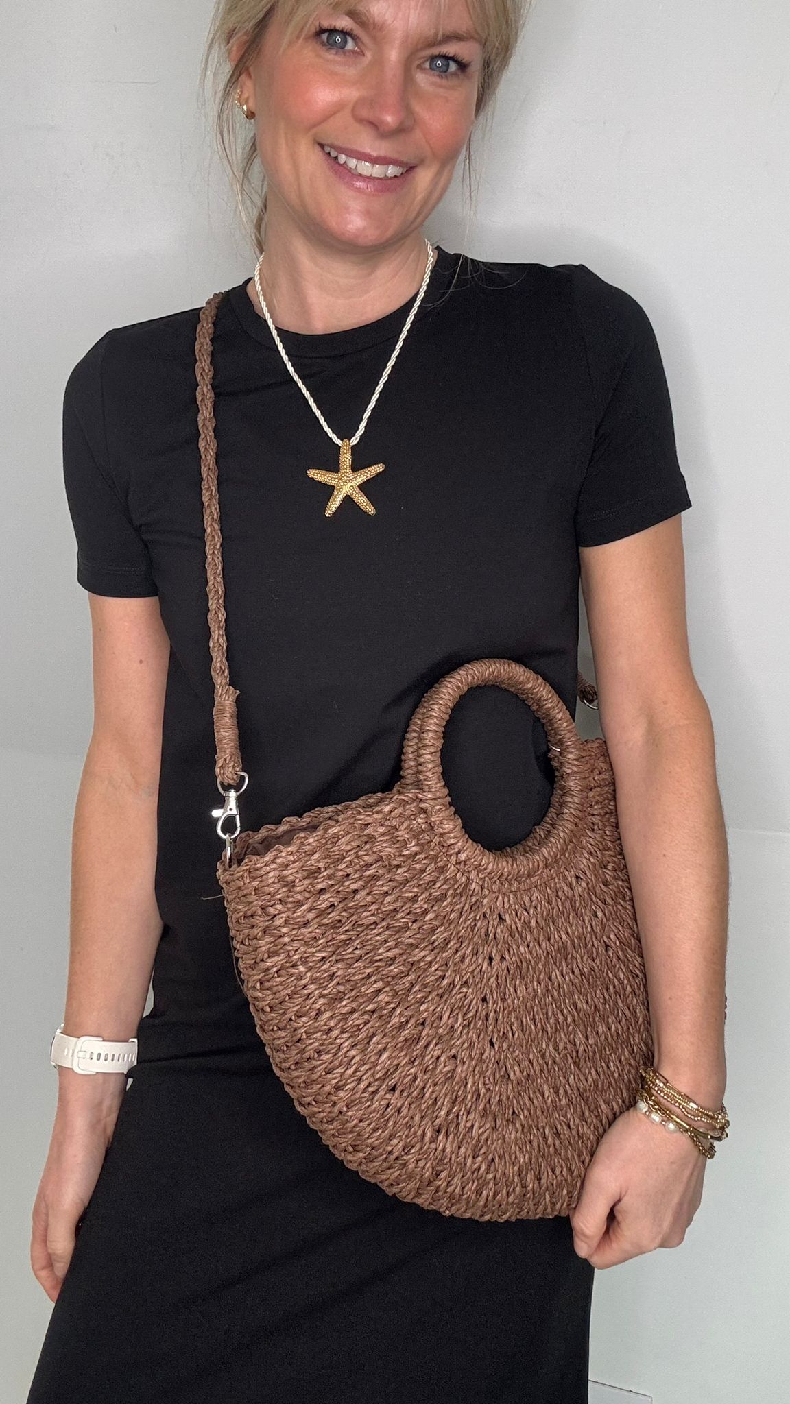 Woman wearing a black dress, holding a brown woven crossbody handbag.
