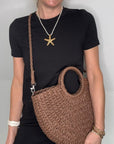 Woman wearing a black dress, holding a brown woven crossbody handbag.