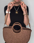 Woman wearing a black dress, holding a brown woven crossbody handbag.