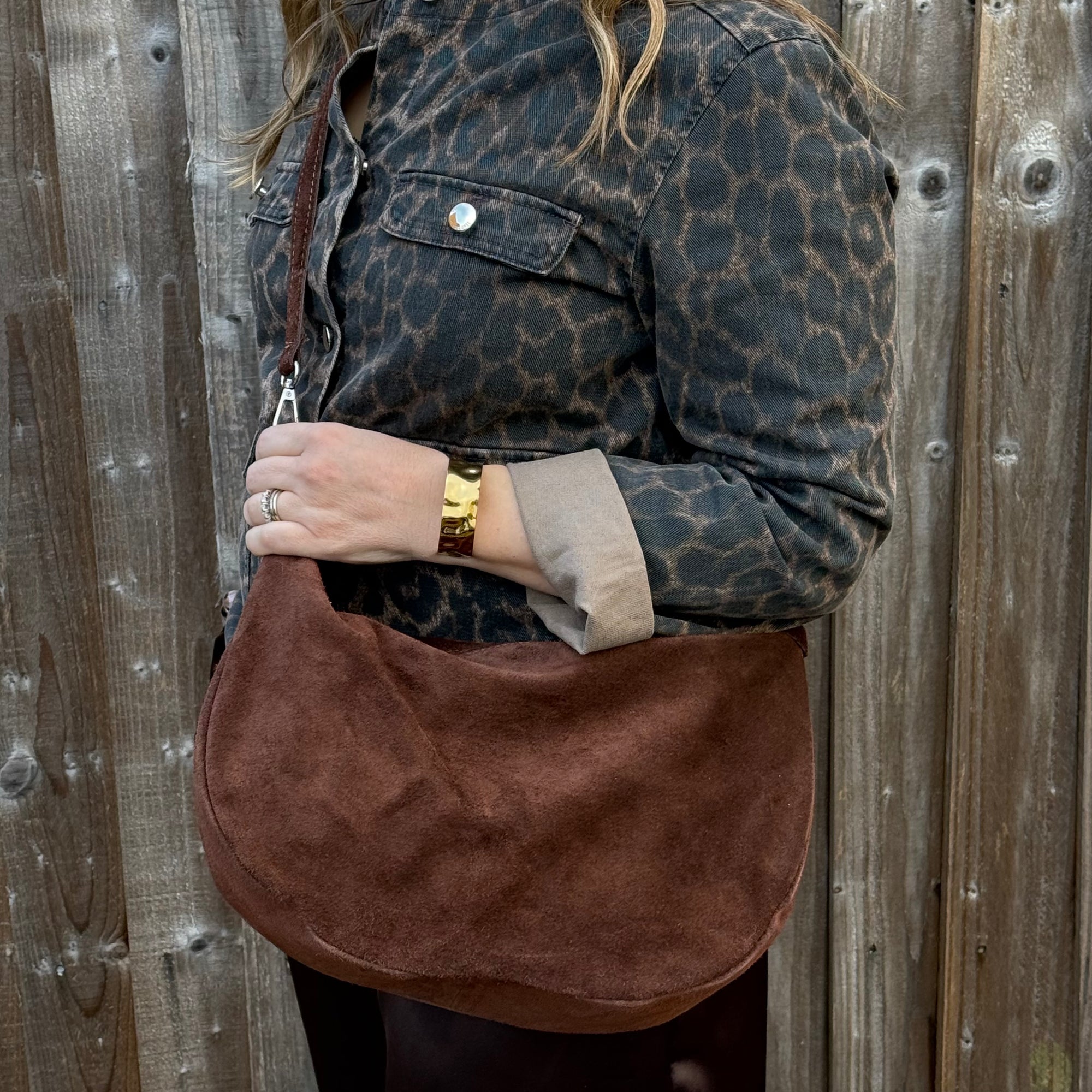 woman holding a brown crossbody bag against a wooden fence