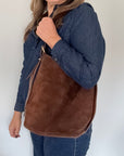 Woman  holding a brown suede shoulder handbag against a white background.