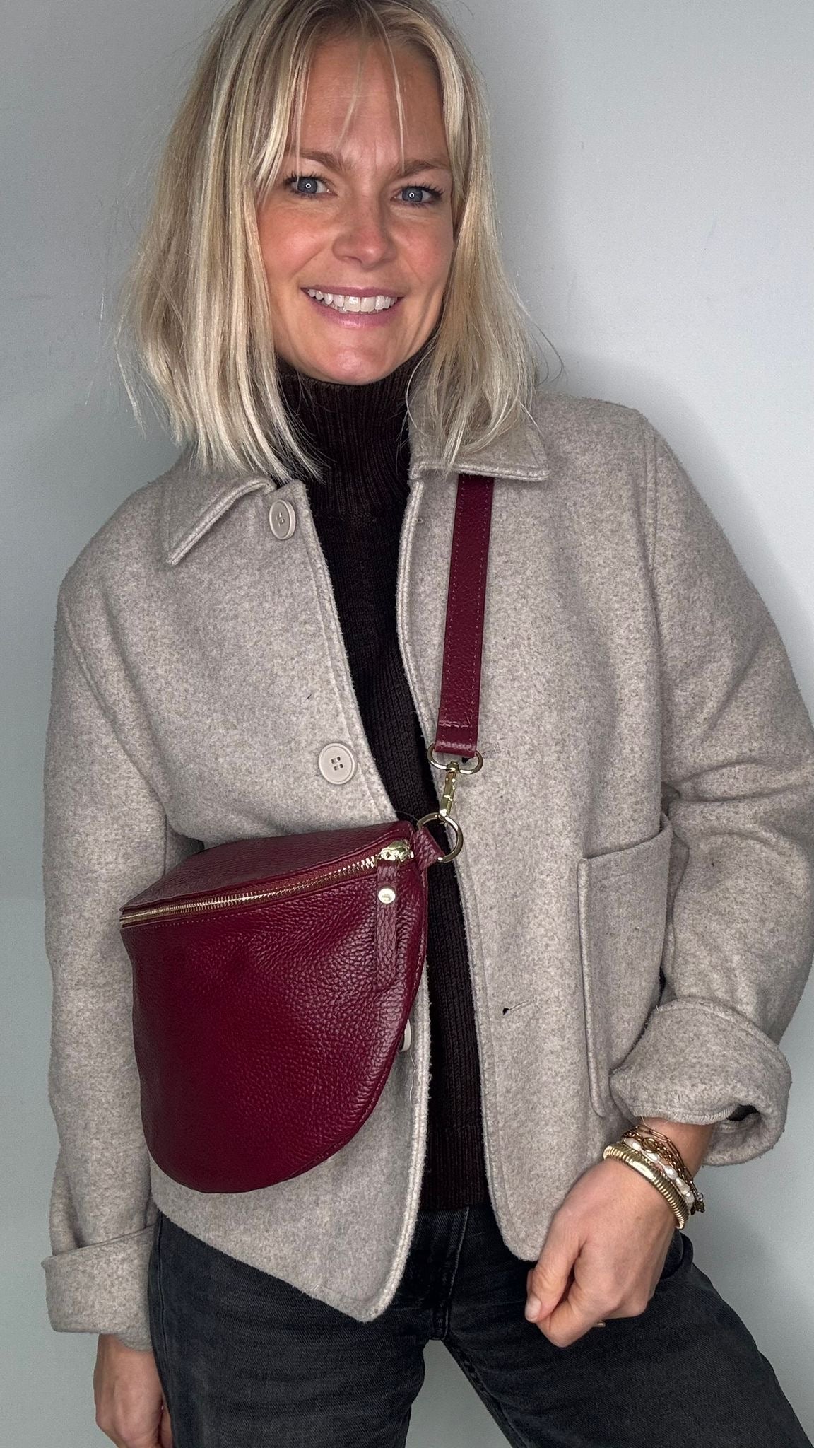 Woman wearing a beige coat with a burgundy deep crossbody / waist bag. 