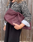 woman wearing a leopard print denim jacket holding a burgundy woven leather textured handbag.