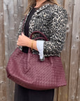woman wearing a leopard print denim jacket holding a burgundy woven leather textured handbag.