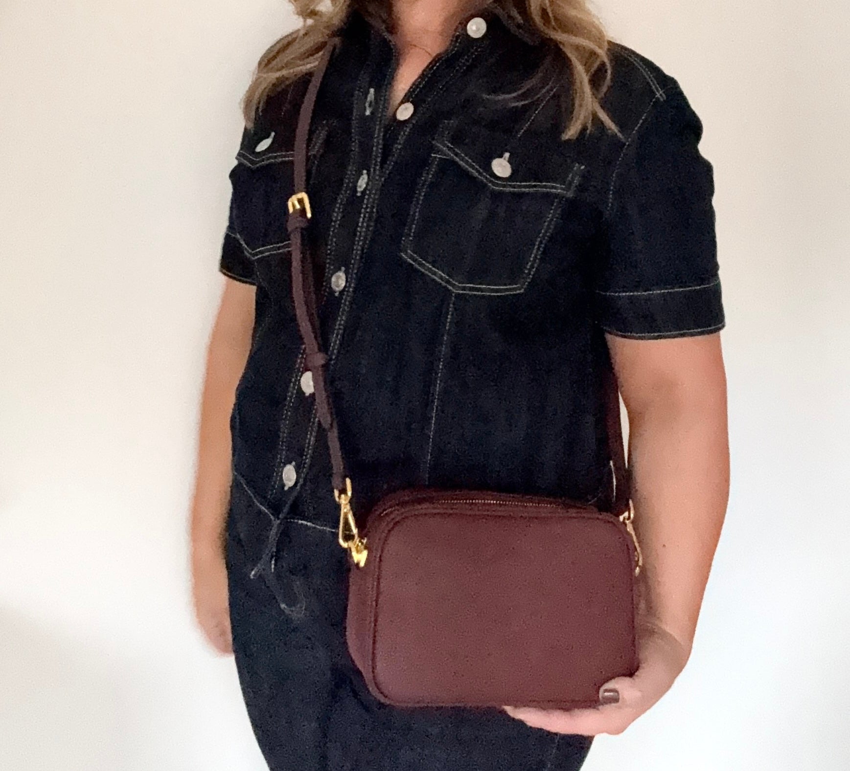 woman holding a burgundy leather crossbody bag with a burgundy leather strap