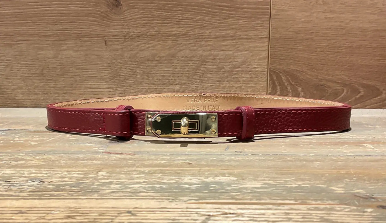 Burgundy narrow leather belt with a gold buckle on a wooden surface