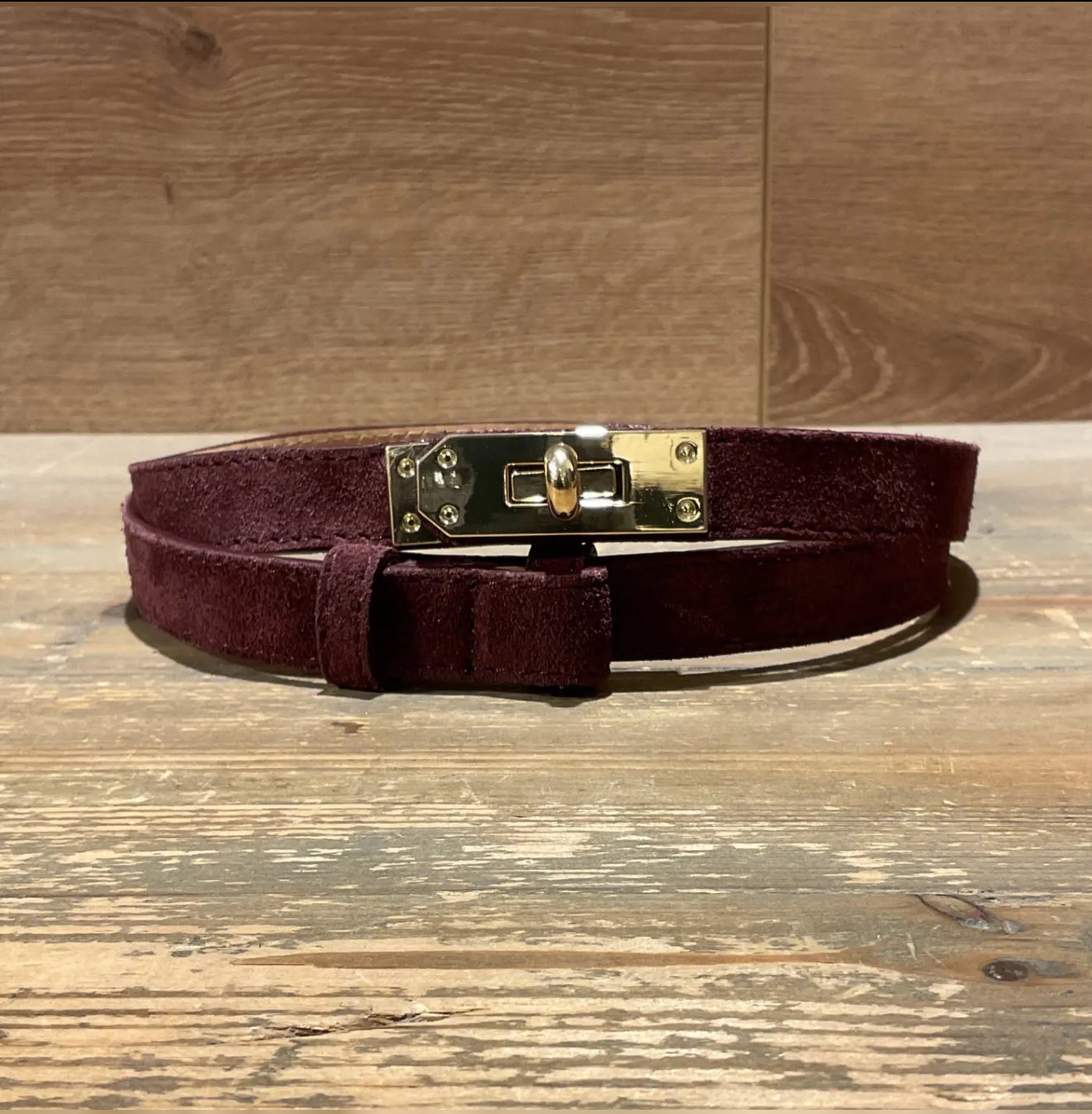 burgundy narrow suede belt with a gold buckle on a wooden surface
