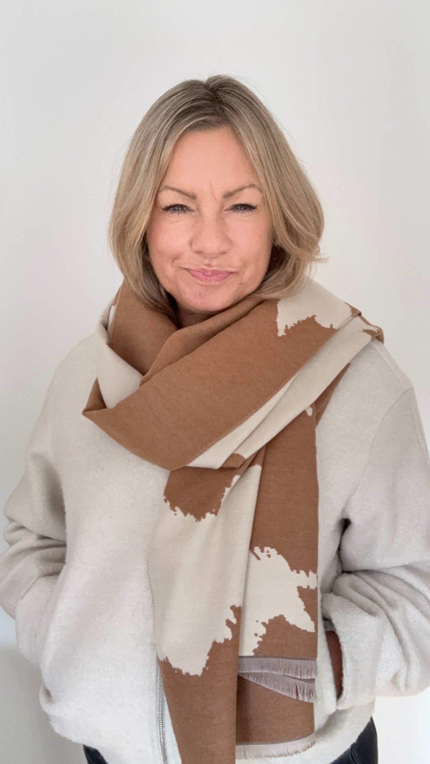 Woman wearing an Autumn Winter camel and cream cow print patterned blanket scarf for layering