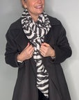 Woman wearing a black coat and a charcoal and white zebra-striped scarf 