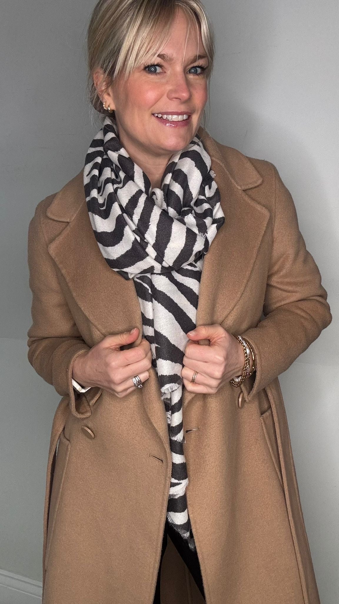 Woman wearing a tan coat and charcoal and white zebra pattern scarf 